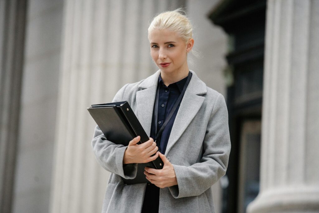 Elegant businesswoman in formal coat holding a folder outdoors in a city setting.